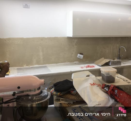 קיר מטבח בשיפוץ עם טיח וכלים על השיש